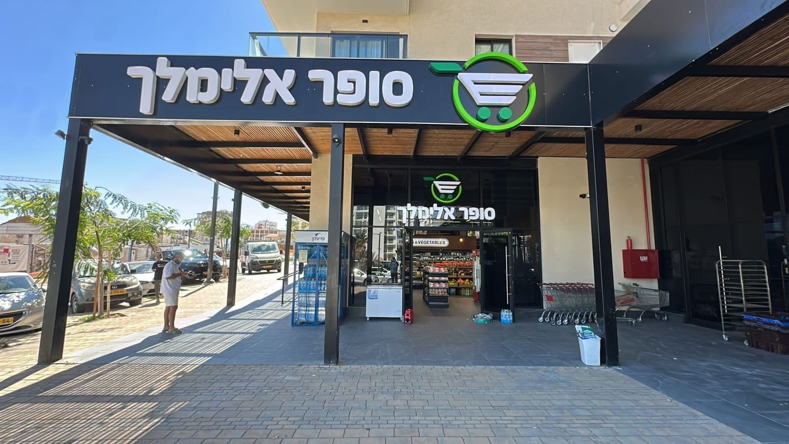 שלט סופר אלימלך עם אותיות לבנות ולוגו עגלה ירוק על גגון הכניסה