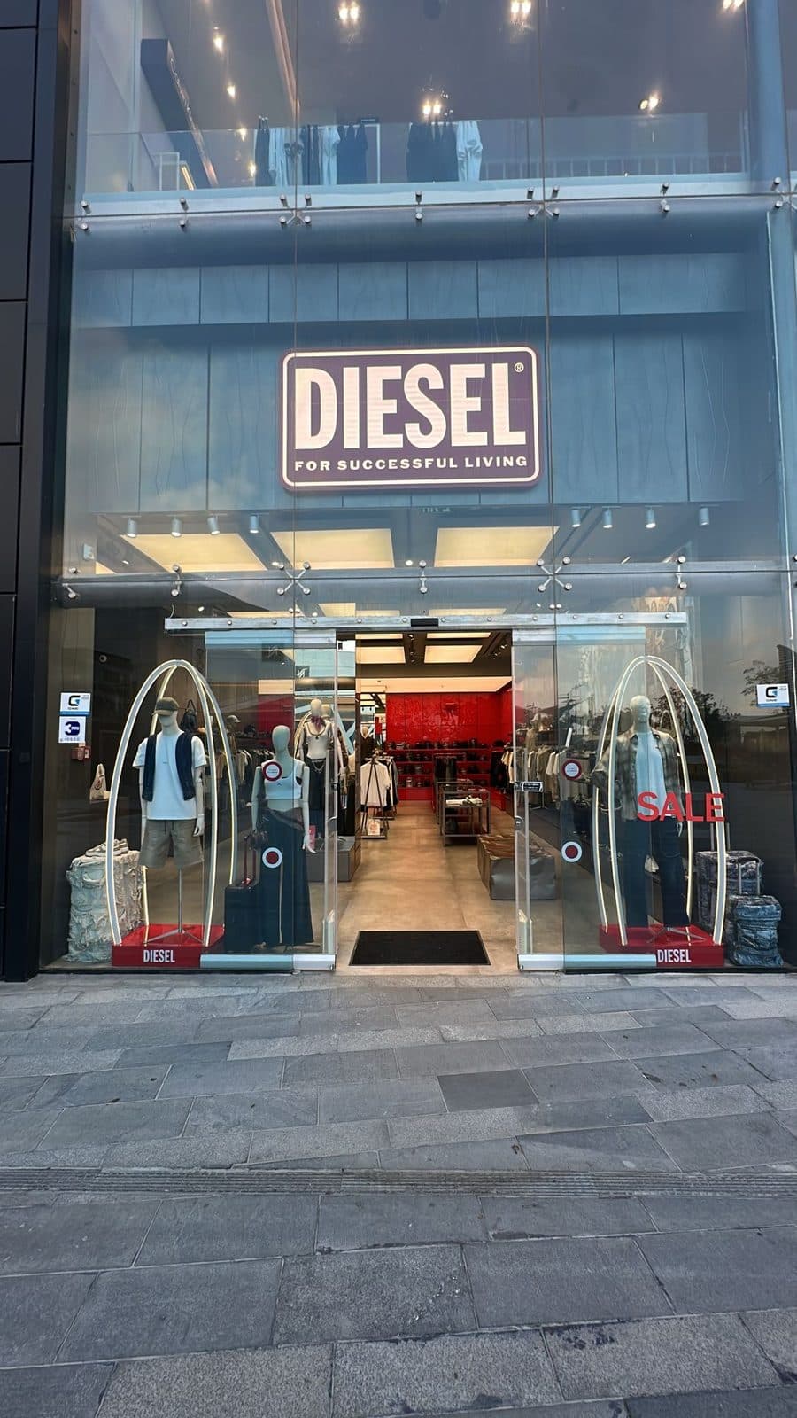 חזית זכוכית של חנות DIESEL בערב — שלט מואר ושתי קשתות תאורה בחלונות