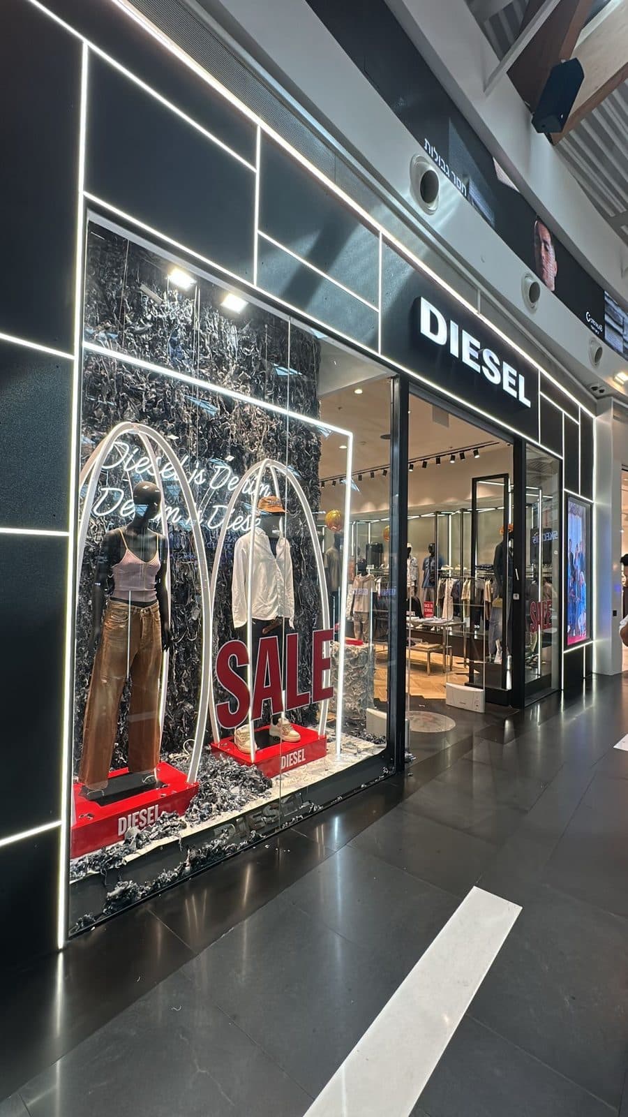 חזית חנות DIESEL בקניון — קירוי שחור עם פסי תאורה, שלט מואר וקשתות ניאון בחלון
